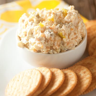 Jalapeno cheese spread in a white cup next to a row of crackers.