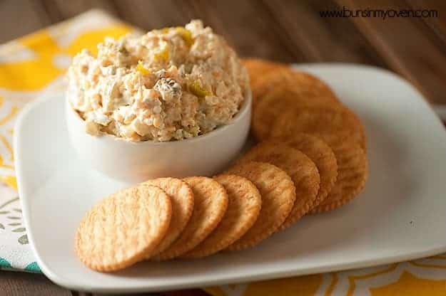 A plate of crackers with a cup of cheese spread.