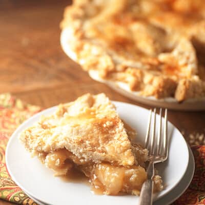 A piece of peach pie on a white plate next to an entire pie.