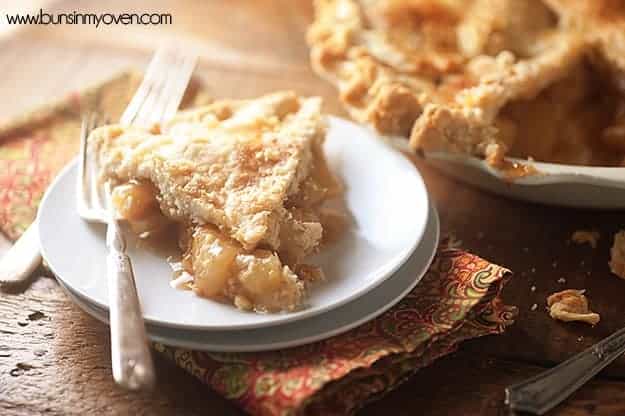 A peach pie on a stacked white plate next to an entire peach pie.