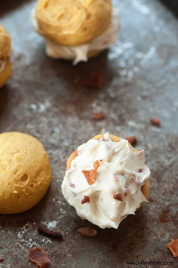 Pumpkin whoopie pies spread out on a baking sheet.