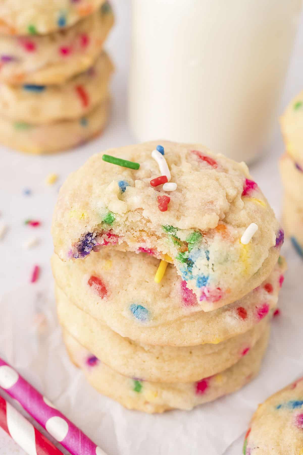 Stack of sprinkle cookies with a bite taken out of the top cookie.