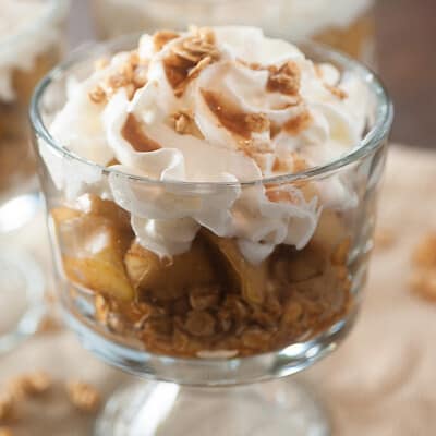 Clear glass cup with apple crisp topped with whipped cream.