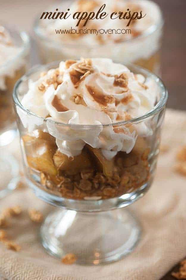 Clear glass cup with apple crisp topped with whipped cream.