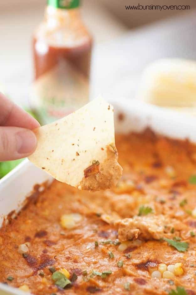 A close up of a person holding a tortilla chip dipped into enchilada dip.