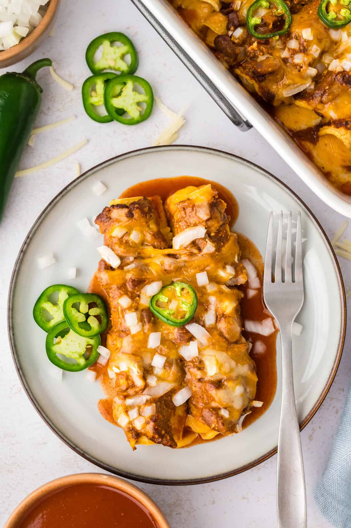 A pan of enchiladas topped with jalapeno and shredded cheese.