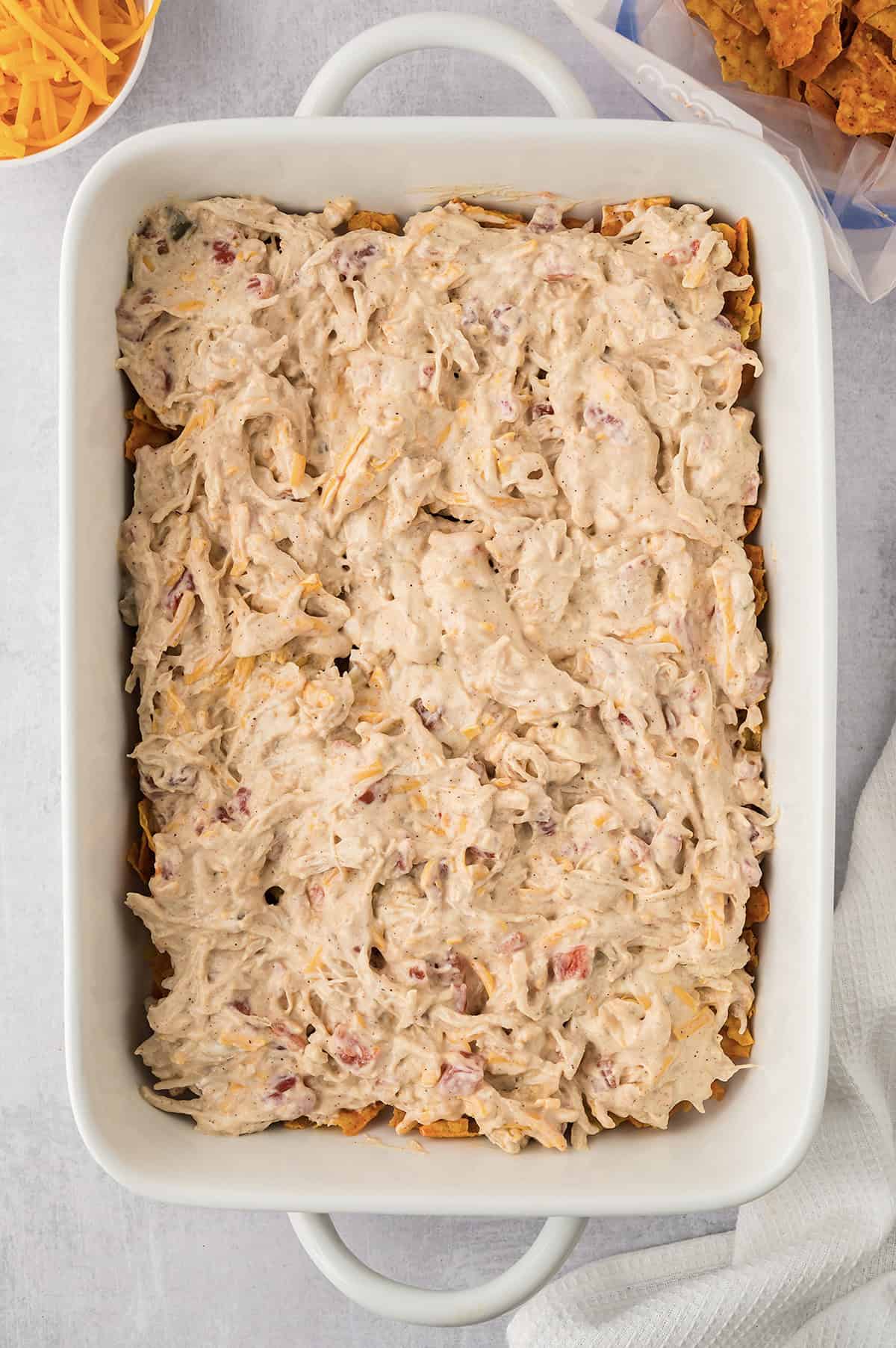 Chicken and sour cream mixture spread over a layer of Doritos in a casserole dish.