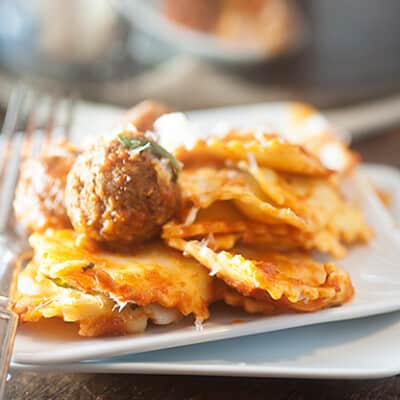 A close up of a plate of ravioli topped with a meatball.