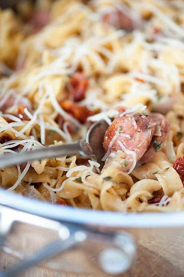 A spoon dipping into a bowl of chicken and noodle pasta.