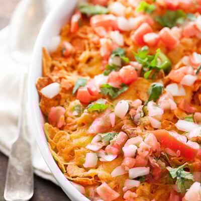 A close up of Dorito pieces, diced chicken and diced onions in a white baking dish.