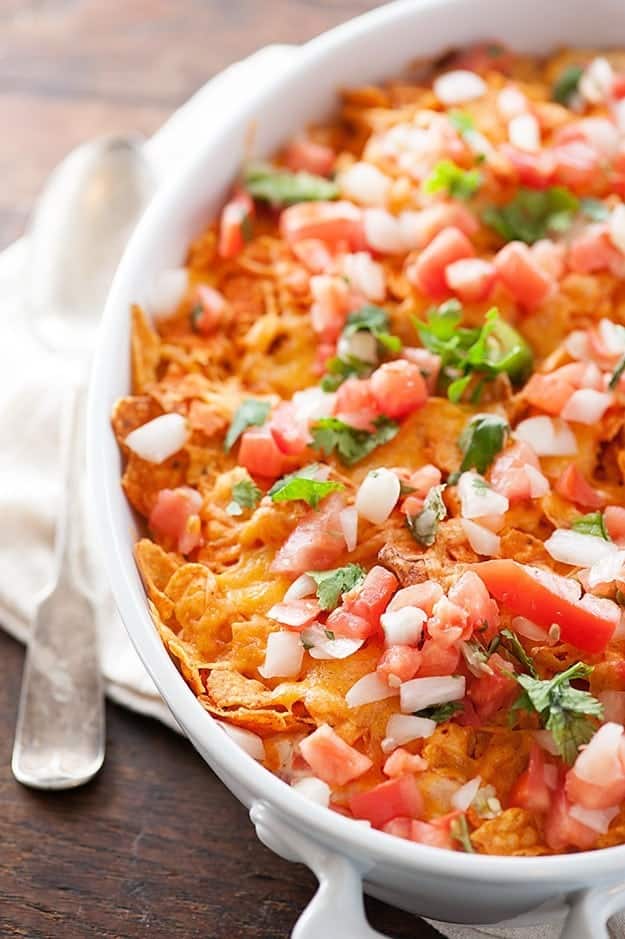 A close up of Dorito pieces, diced chicken and diced onions in a white baking dish.