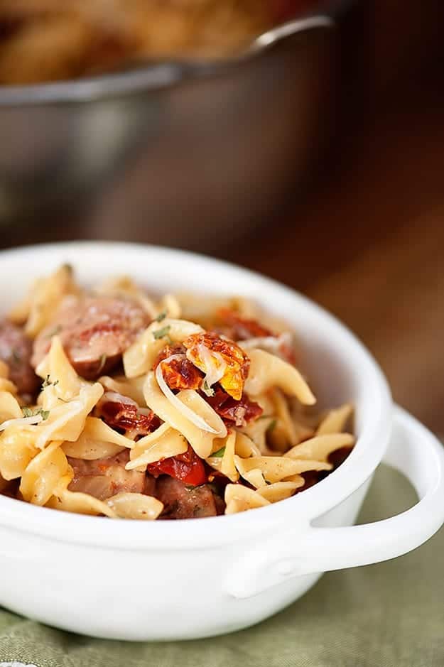 A cup of chicken and noodle pasta with dried tomatoes.