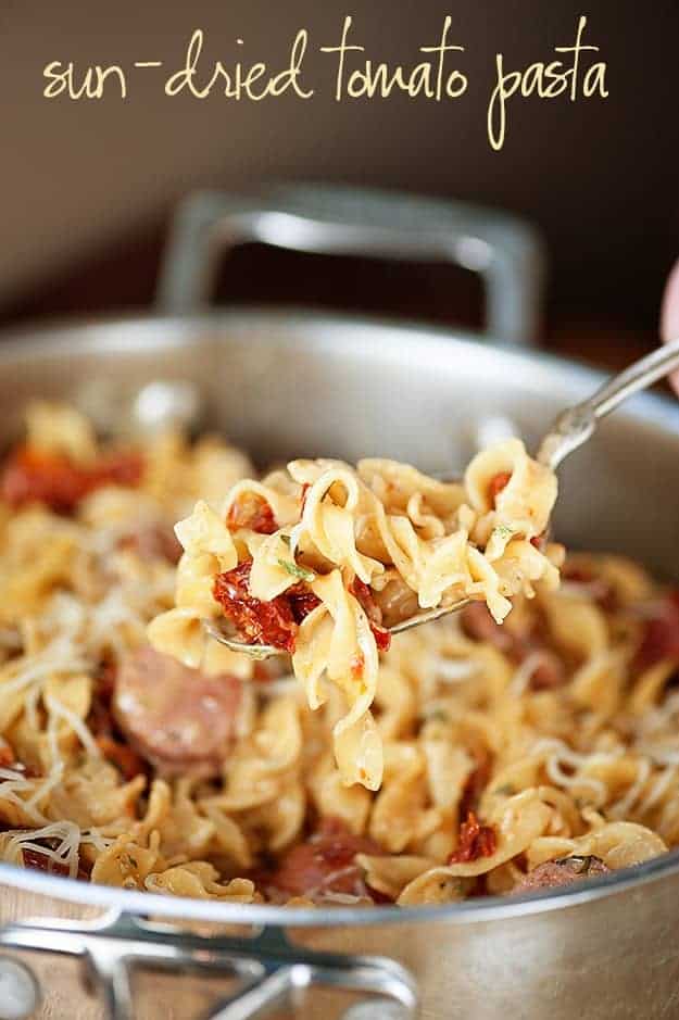 Chicken and pasta on a spoon held up above a pot of pasta.