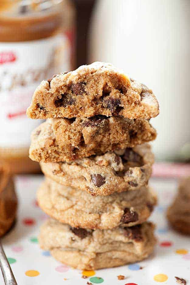 A close up of stacked up chocolate chip cookies where the top two cookies are cut in half on a wooden table.
