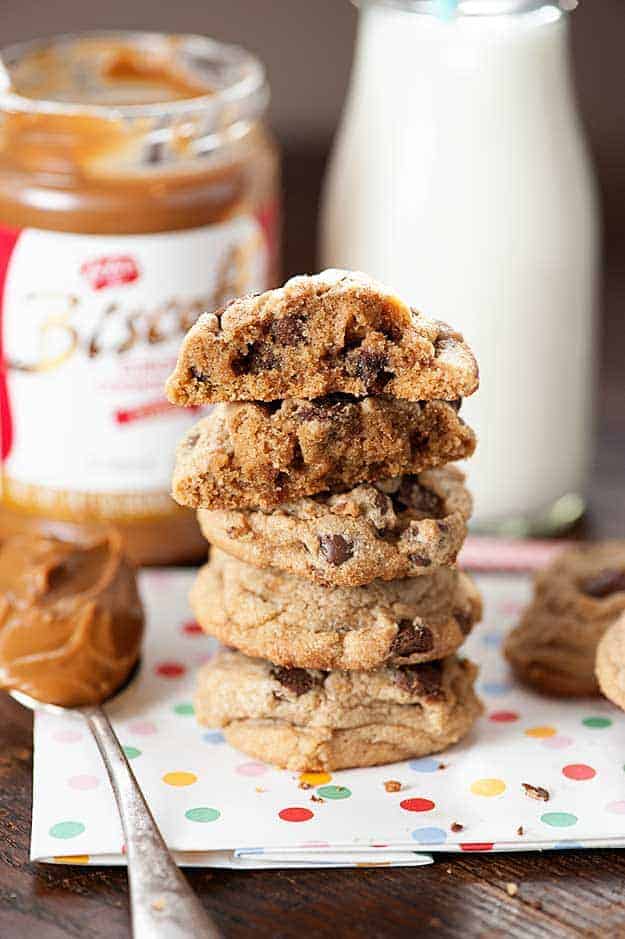 Stacked up chocolate chip cookies where the top two cookies are cut in half in front of a jar of biscoff.