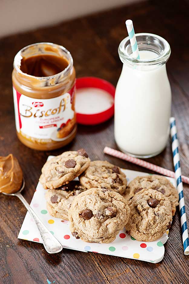 A jar of biscoff and a jar of milk on a table with a plate of chocolate chip cookies.