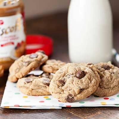 A few chocolate chip cookies on a folded cloth napkin in front of a jar of milk.