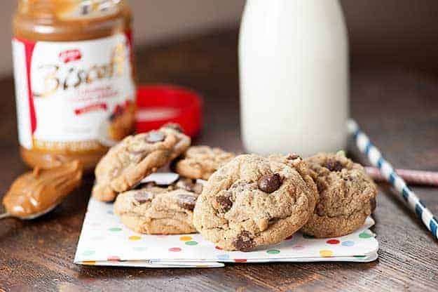 A few chocolate chip cookies on a folded cloth napkin in front of a jar of milk.