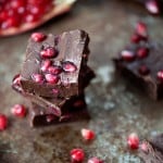 A bunch of fudge squares in front of a bowl of pomegranate on a table.
