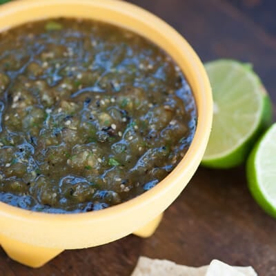 A cup of salsa and lemon halves on a wooden table.