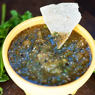 A tortilla chip dipped into a bowl of salsa verde.