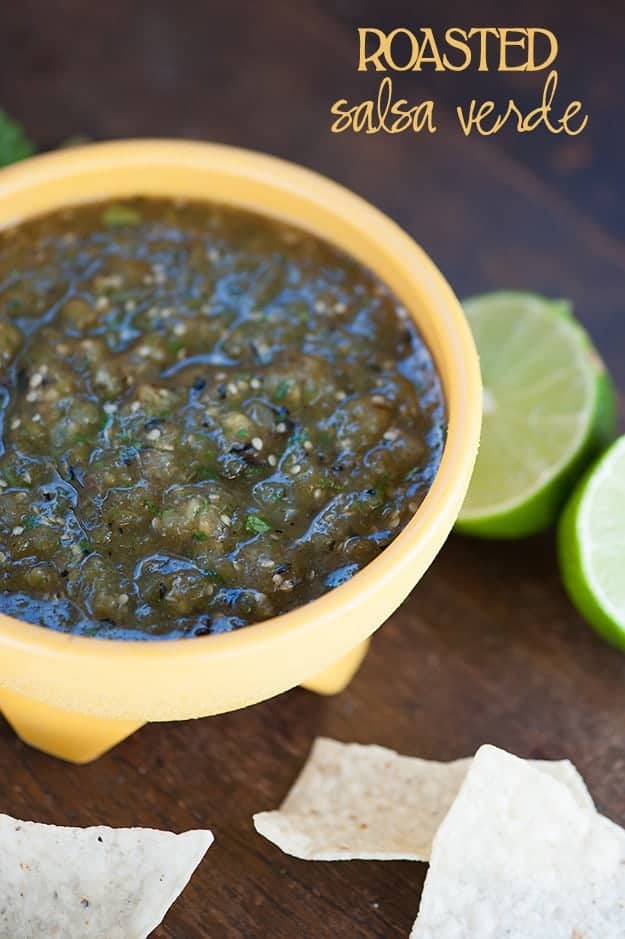 A cup of salsa and lemon halves on a wooden table.