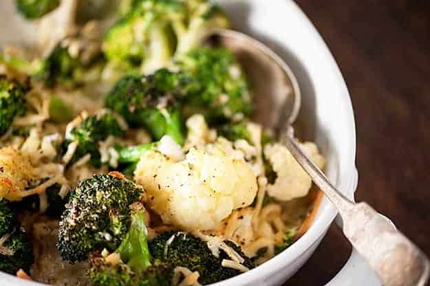 Cauliflower and broccoli in a white bowl with a silver spoon.