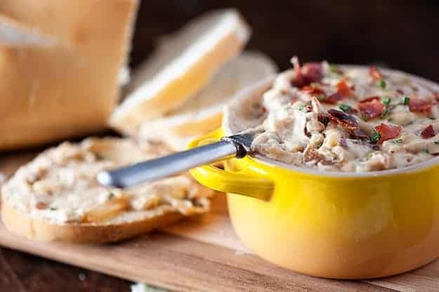 A knife in a cup of onion dip in front of a loaf of bread.