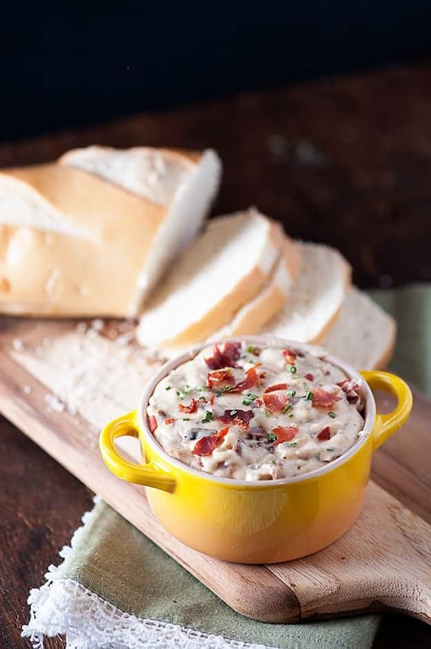 French bread on a cutting board next to a small cup of onion dip.