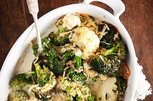 A white baking pan of broccoli and cauliflower with shredded cheese.