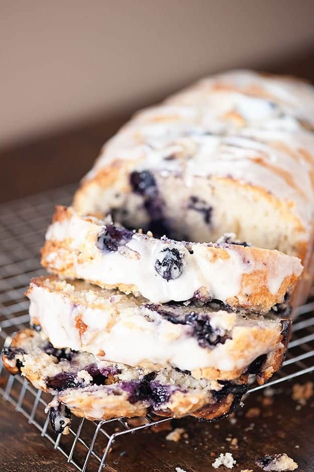 A loaf of blueberry muffin bread cut into slices on a wire cooling rack.