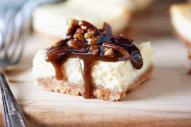 Cheesecake square topped with chocolate syrup on a wooden cutting board.