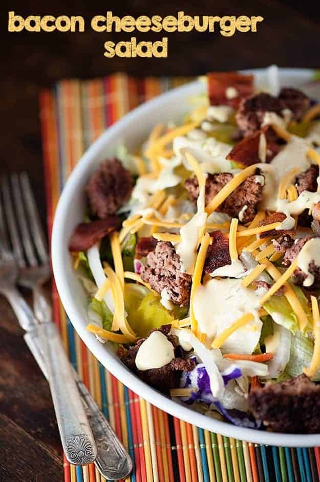 A white bowl of salad topped with bacon and shredded cheese on a striped cloth napkin.