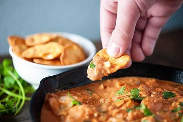 A close up of a person holding a naan crisp above a chicken dip.