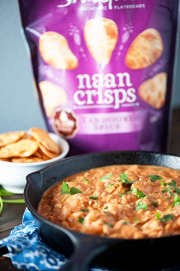 Indian butter chicken in a cast-iron skillet in front of a bag of naan crisps.