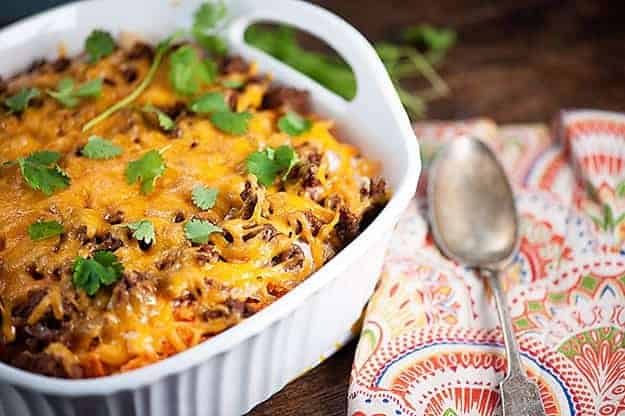 A white baking dish full of cheesy casserole next to a cloth napkin.