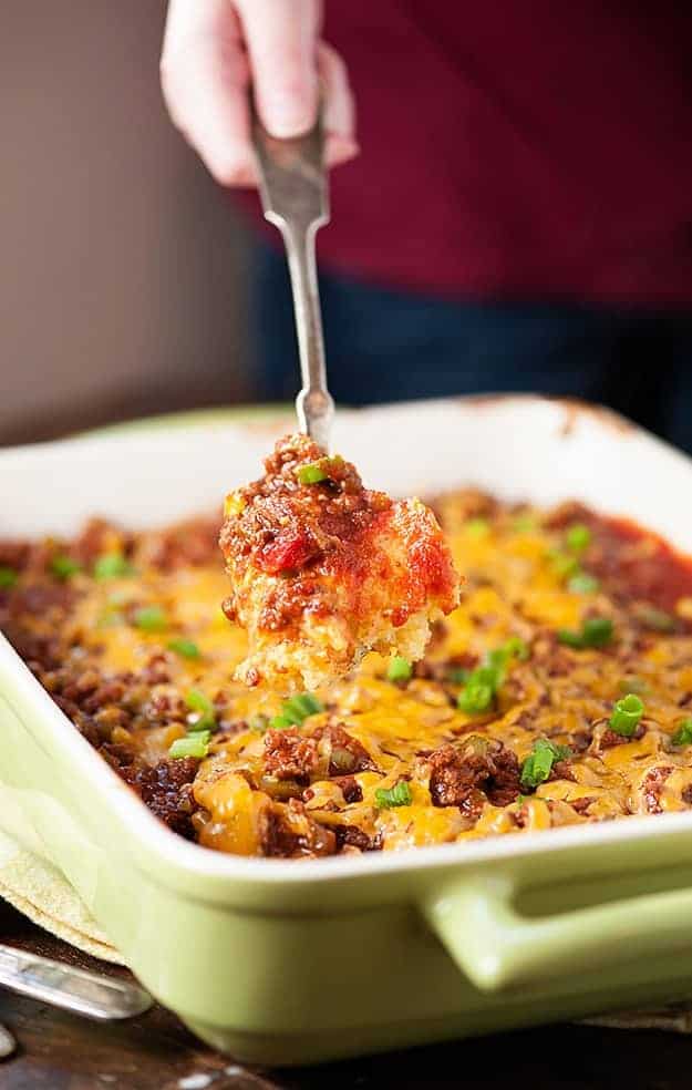 A spoon holding up a scoop of sloppy joe casserole above a baking dish.