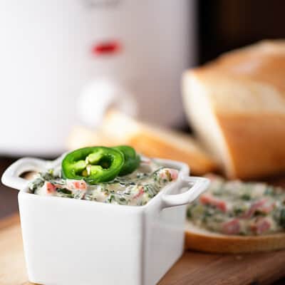 A square dipping tray full of spinach dip topped with jalapenos.