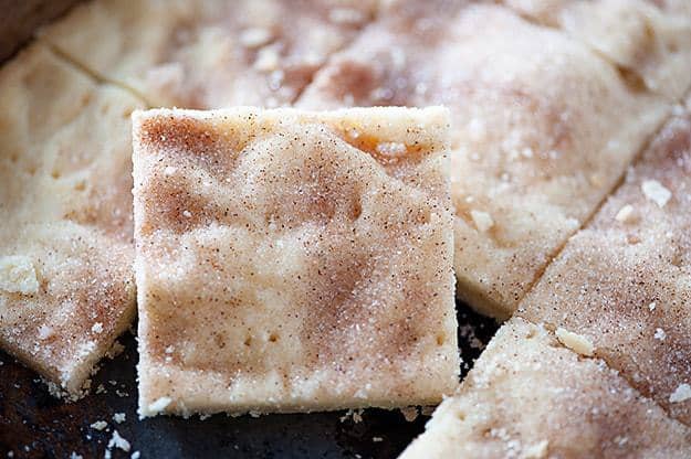 A close up of a square of shortbread cut out of a baking sheet full of shortbread.