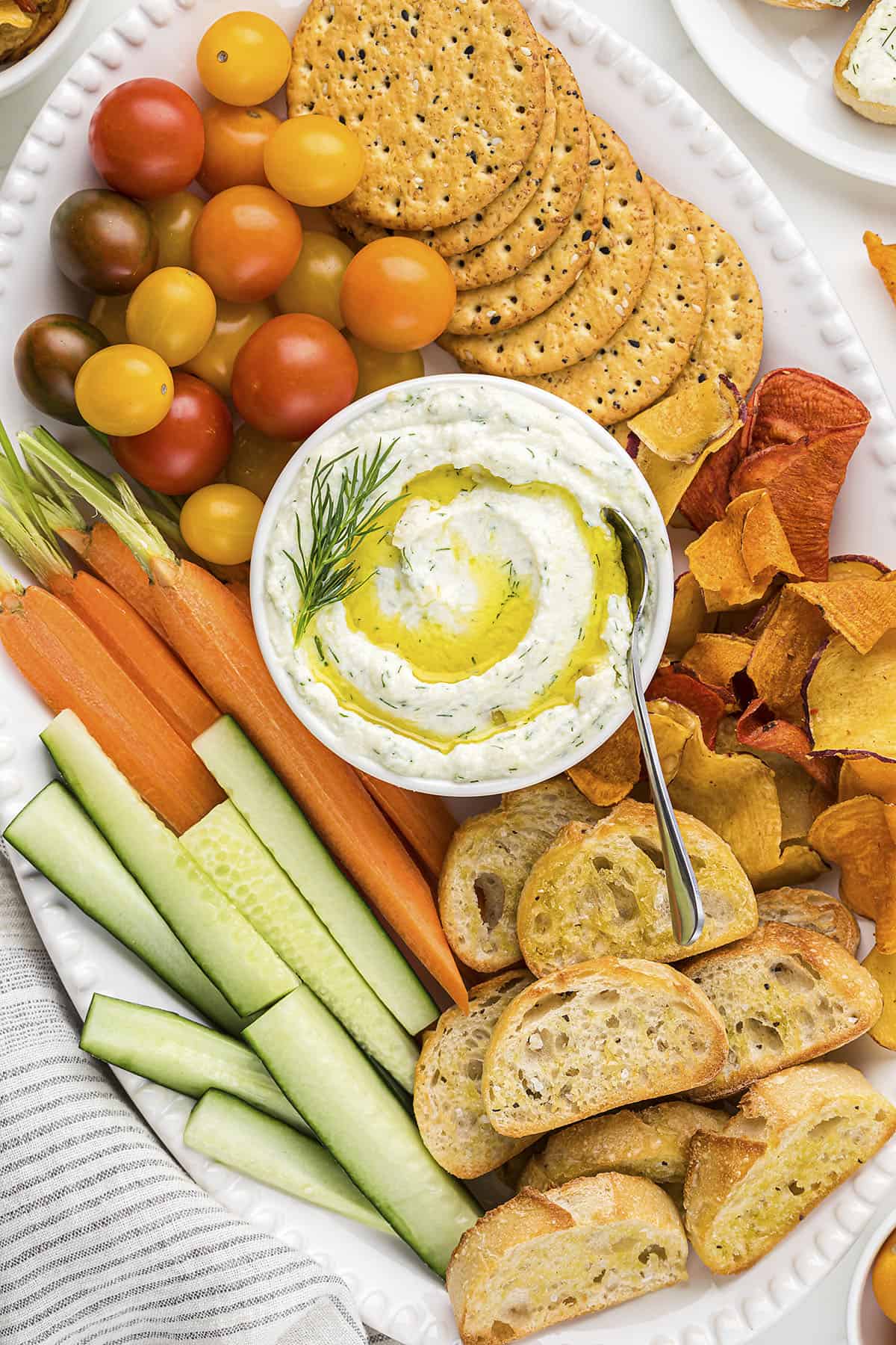 Ricotta dip in bowl surrounded by fresh vegetables and crackers.