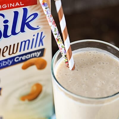 A glass of peanut butter smoothie next to a container of silk milk.