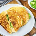 Grilled cheese sandwich stuffed with jalapenos on white plate.