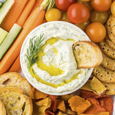 Garlic ricotta dip in white bowl surrounded by fresh vegetables.