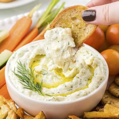 Hand dipping a piece of crositin into garlic ricotta dip.