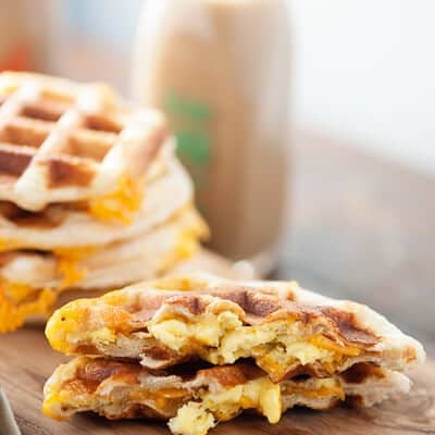 A close up of a cut in half waffle on a cutting board in front of a stack of waffles.