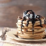 A stack of pancakes topped with chocolate syrup and chunks of peanut butter cups.