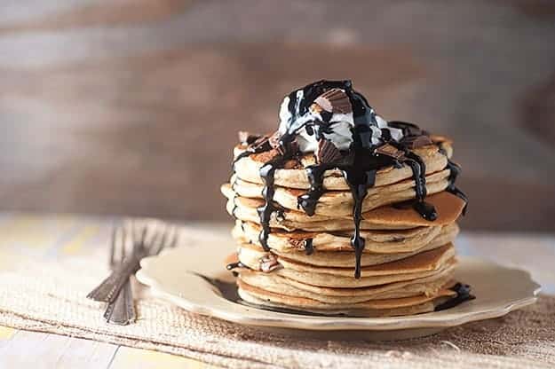 A stack of pancakes topped with chocolate syrup and chunks of peanut butter cups.