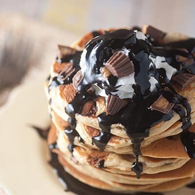 Overhead view of chocolate syrup and peanut butter cups on a stack of pancakes.