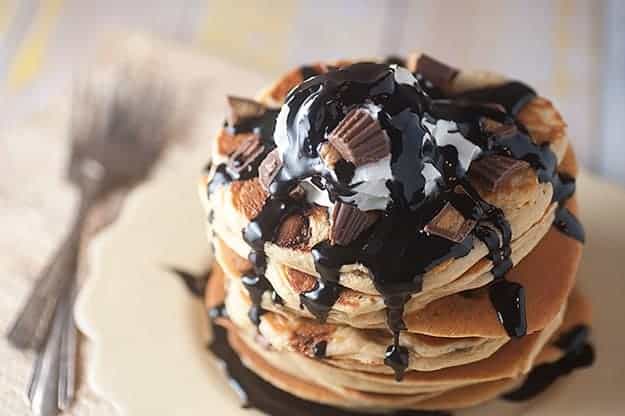 Overhead view of chocolate syrup and peanut butter cups on a stack of pancakes.