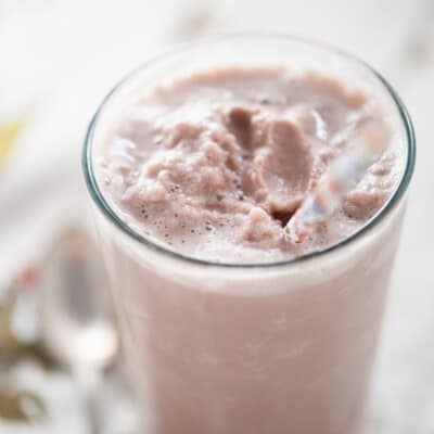 A protein shake in a clear glass with a straw in it.